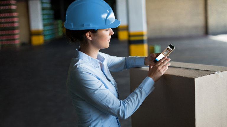 Female factory worker using mobile phone with barcode scan